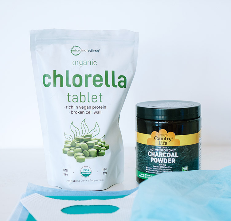 A bag of Micro Ingredients organic chlorella tablets, a jar of Country Life activated charcoal powder, and a protective blue dental drape used during a safe SMART mercury removal protocol.