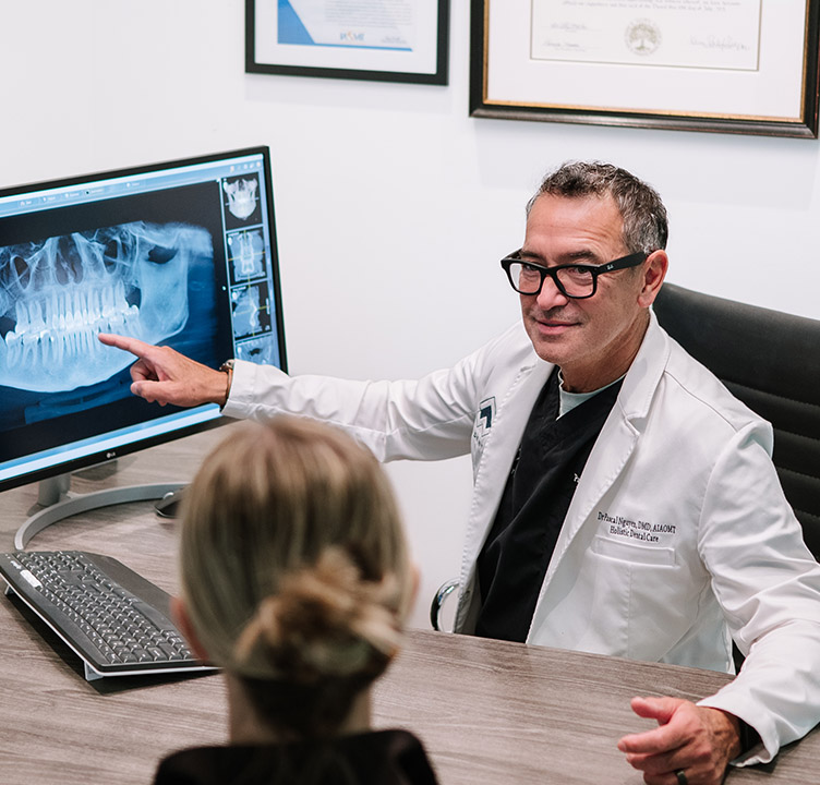 Dr. Pascal Nguyen of PJN Dental points to a digital panoramic jaw X-ray on a monitor while consulting with a patient about a safe tooth extraction.