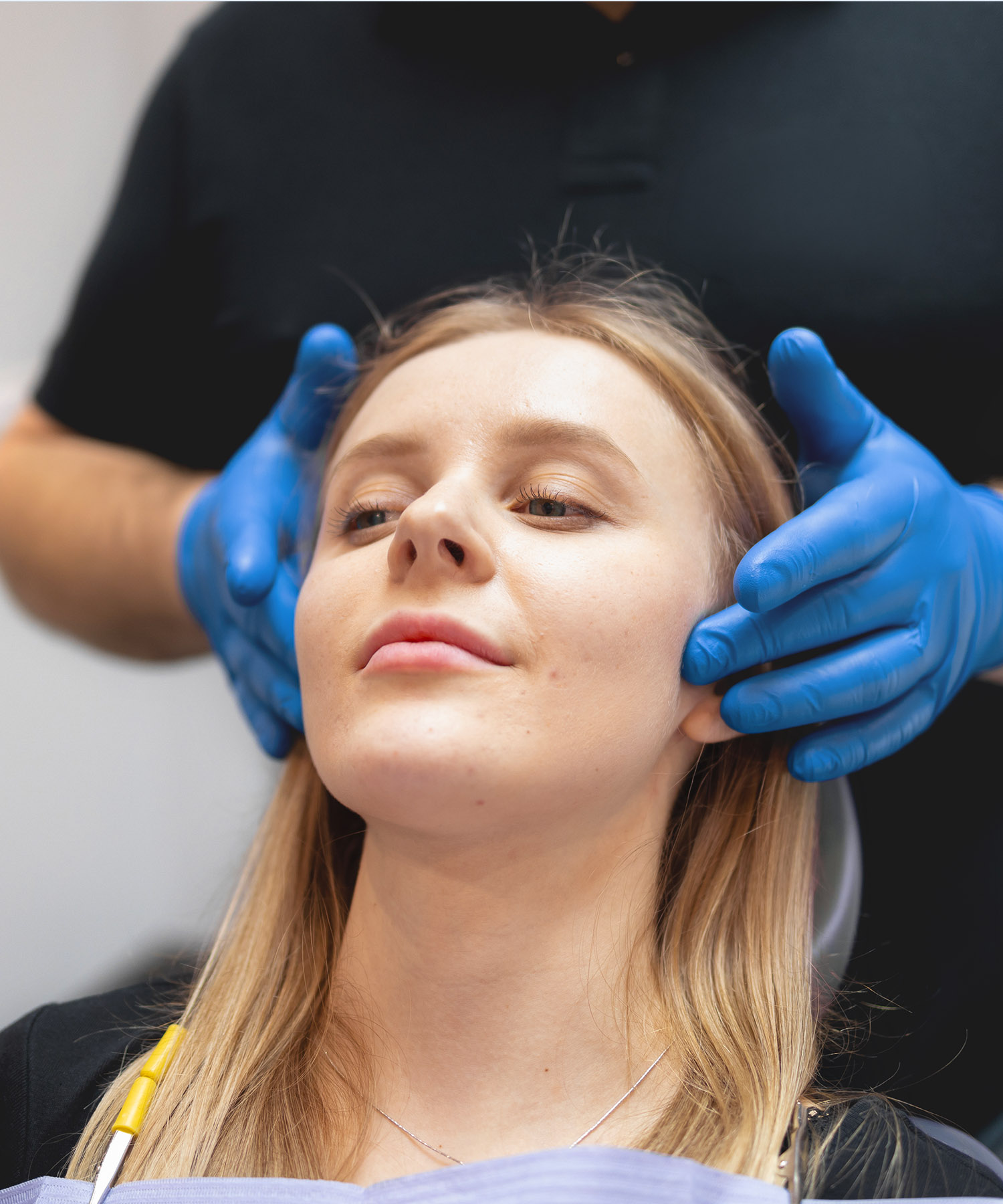 Dr. Pascal wearing blue gloves gently palpates a female patient's jaw muscles and temporomandibular joint (TMJ) during a functional bite evaluation.