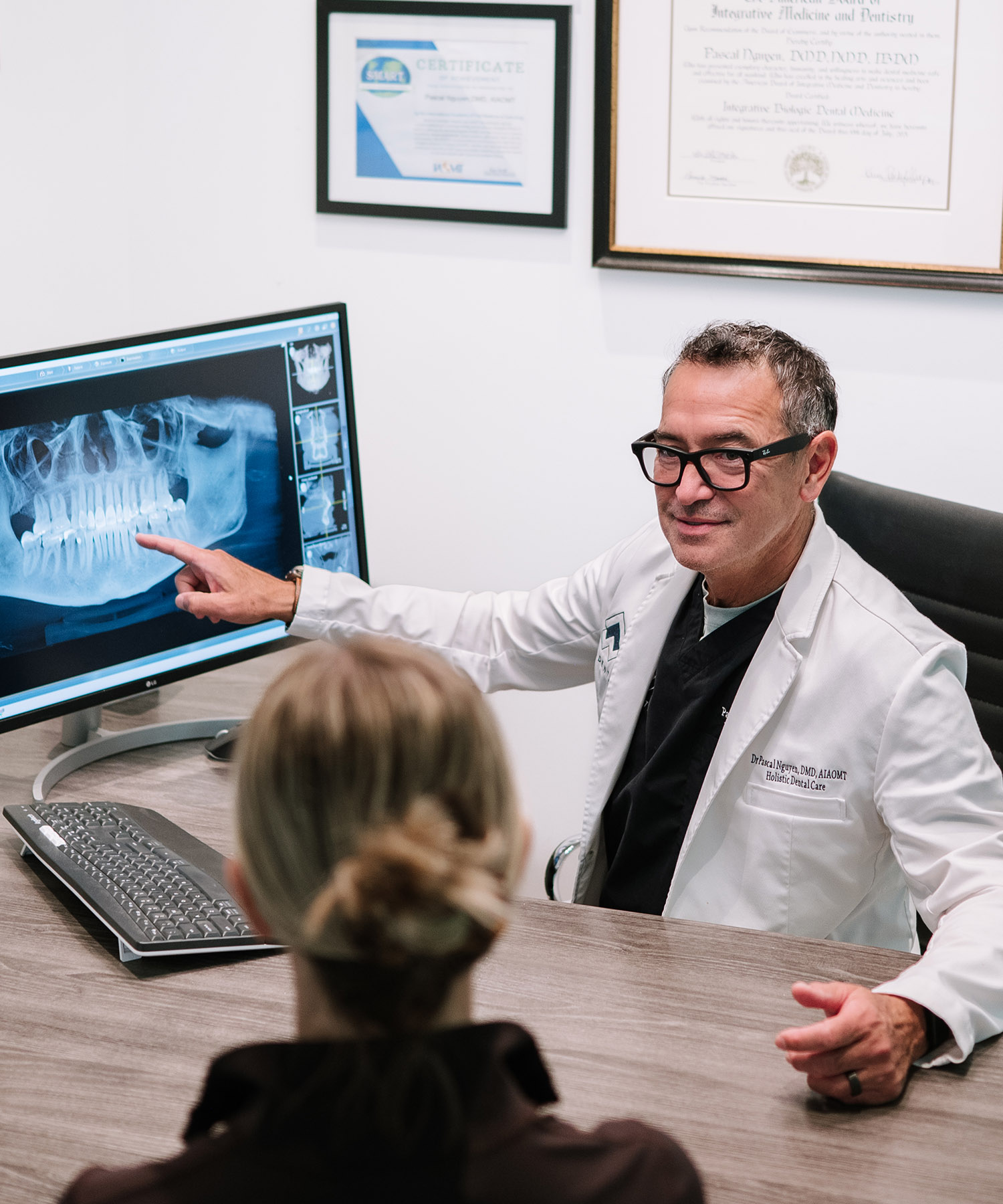 Dr. Pascal Nguyen of PJN Dental points to a digital panoramic jaw X-ray on a monitor while consulting with a patient about a safe tooth extraction.
